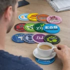 Man holding coffee with Kalex PVC Coasters arranged colorfully on a wooden table.