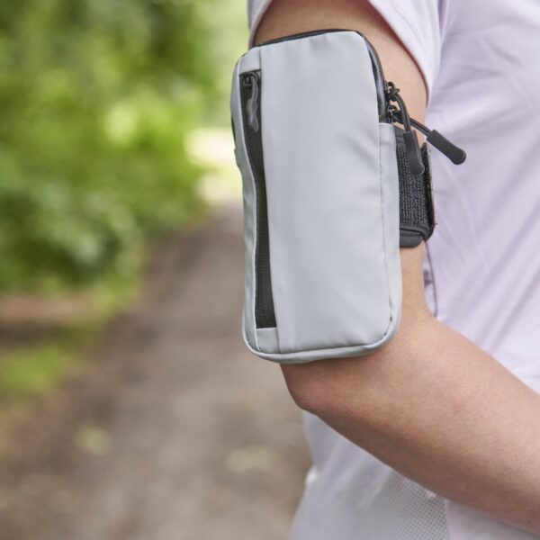 Person wearing a Christel Arm Bags white armband pouch outside with greenery behind.