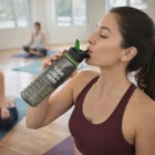 Woman in workout gear drinks from Olly Drink Bottle at yoga class.