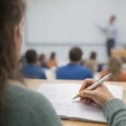 Student taking notes with Artella Pens White Barrel, focused on the lecturer at the front.
