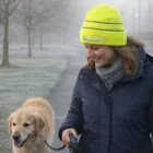 Woman in a Hi-Vis Cuff Beanie Cap walks a golden retriever on a misty path.