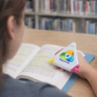 Someone uses Trio Highlighters to mark a book in a library with various stationery nearby.