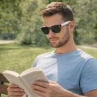 Man wears Moana Premium Sunglasses White and reads a book outdoors on a sunny day.