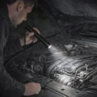 A person uses a Swiss Peak Engraved Logo Torch to inspect a car engine at night.