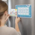Placing a child's drawing in a 17x13cm Photo Frame Fridge Magnet beside a blue calendar.