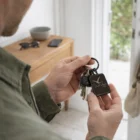 Person holds keys with a black Manolo Rectangle Keyring near a wooden table by the door.