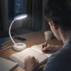 Person studies at a desk under a Foldable Lamp, writing in a book at night.