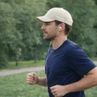 Man jogging wearing Event Sports Branded Cap, blue shirt, and earphones in a park.