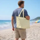 Man carries Frosty Cooler Bag in yellow while walking on sandy beach near ocean.