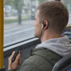 A man with Gator Bluetooth Earbuds sits on a bus, looking out the window with a remote.