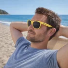 Man relaxing by the ocean, wearing Colour Changing Sunglasses on a beach chair.