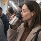 Woman sipping from a Radel 380Ml Double Wall Flask on a crowded subway train.