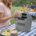 Woman places sandwiches in a felt bag at a picnic, with her family in the background.