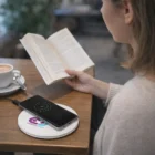 Woman reads as her phone charges on a Tala Wireless Charger at the table.