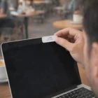 Person attaching Cheap Laptop Webcam Cover to laptop screen in a café.