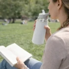 Woman reads a book and sips from Ochoa Glass Bottles Neoprene Sleeves in the park.