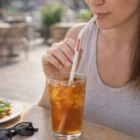A woman sips iced tea with Reusable Silicone Straws at an outdoor table, sunglasses beside her.