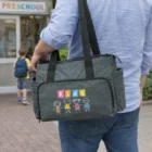 Person holding Junior Logo Branded Baby Bag outside preschool, child ahead with backpack.