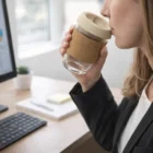 Woman drinks from a 340Ml Eco Cork Band Promo Cup while working at her computer desk.