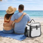 A couple relaxes on a beach towel by the ocean with a Siamo Cooler Bag at their side.