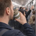Man sipping from a Tastee Cups 480Ml on a crowded train, ditching disposable cups.