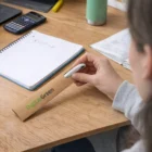 Person holding a pen with Riza Cardboard Pen Sleeves at a desk with books and a calculator.