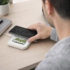 Someone sets a phone on an Autonoe Wireless Charger labeled "Fresh Ideas" on a desk.