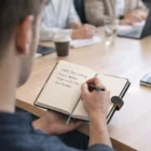 Writing meeting notes in Corporate Notebooks With Magnetic Closure at a conference table.
