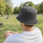 Person wearing Coloured Trim Event Bucket Hat sits on grass in a park, seen from behind.