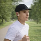 Man jogging outdoors in a white tee, Class Cord Trucker Cap, and wireless earbuds.