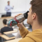 In a classroom, someone drinks from a Mexxa Vacuum Bottles Stainless Deco with a surf sticker.