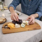 Someone arranges grapes and cheese on Homegoods Serving Boards with bread and wine at the table.
