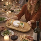 Smiling woman serves cheese on a Nice Cheese Board at a cozy candlelit dinner table.