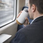 Man drinks from a Kostner Vacuum Cup while sitting by a train window.