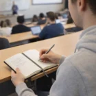 Student takes notes with College Style Logo Decorated Notebooks in a lecture hall.