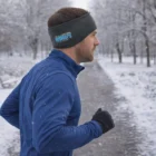 Man jogging on snow, in a blue jacket, gloves, and Giorgio Ear Warmers.