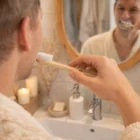 Man brushing teeth with Toothbrushes Bamboo, reflected in the bathroom mirror.