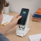 A person places a phone showing 75% charge on an Aqui Wireless Charging Stand on a desk.