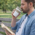 Man on a bench sipping from a Brewster Cups Double Wall, reading a book in the park.