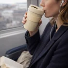Woman sips from a Brewster Cups Natural while reading a book on the train.
