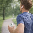 Man jogging in park, wearing Precision Bluetooth Earbuds and holding Oak Tree Daily Gummies.