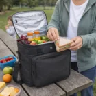 Someone at a picnic grabs a sandwich from a Shelton 16L Personalised Cooler Bag stocked with snacks.