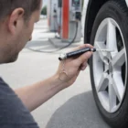 Person checks car tyre pressure with a Bulk Tyre Gauge Keyring at a gas station.