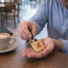 Person holding keys with an Alta Key Rings Square at a café, coffee nearby.