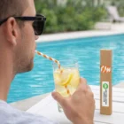 Man by pool drinks lemon water with Zetty Paper Drinking Straws; box on table nearby.