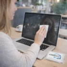 Woman cleaning laptop screen with Zenno Microfibre Cleaning Clothes at a wooden café table.
