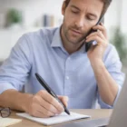 Man writing notes with an Essen Customised Pen while on the phone at his desk.