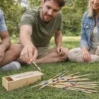 Three people playing Personalised Wooden Pick Up Sticks Games on grass with a branded box.