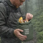 Wearing rain gear, a person grabs snacks from a Huxley Dry Bags- 5L outdoors.