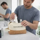 Man putting toiletries in a beige and brown Paisleigh Toiletry Bag with YOUR LOGO HERE text.